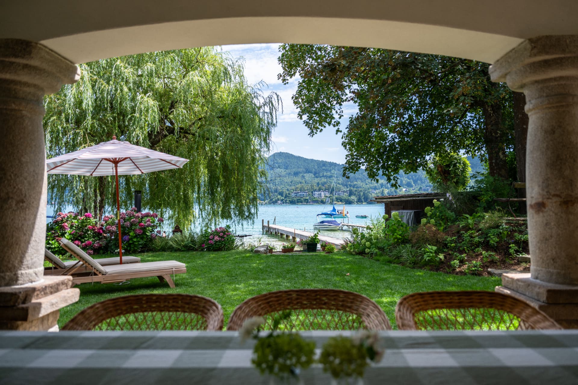 Blick von der überdachten Terrasse durch den Garten auf den Wörthersee